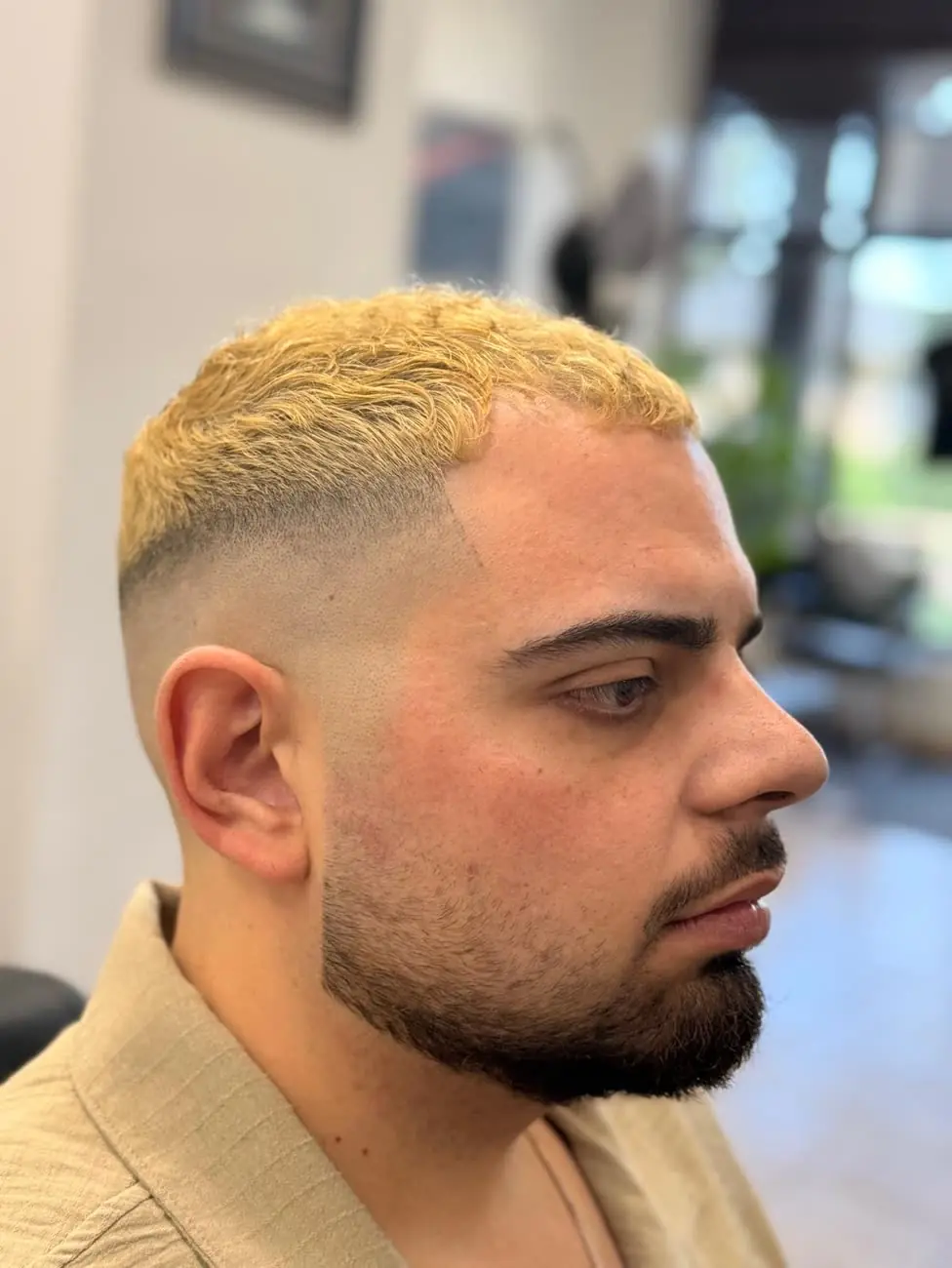 Side view of a client at Tony Matee's with a bleached textured crop, a skin fade above the ear and a lined-up beard