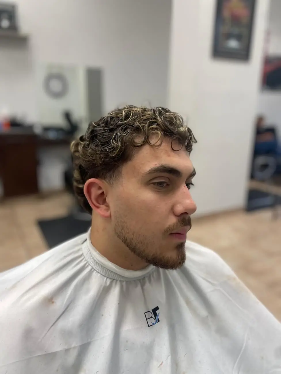 Curly top with light highlights, a tapered side and a shaped beard